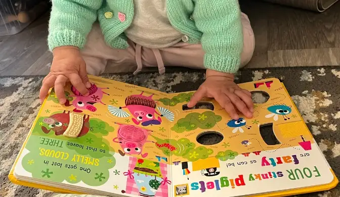 A baby turning the pages of a colourful board book on the floor