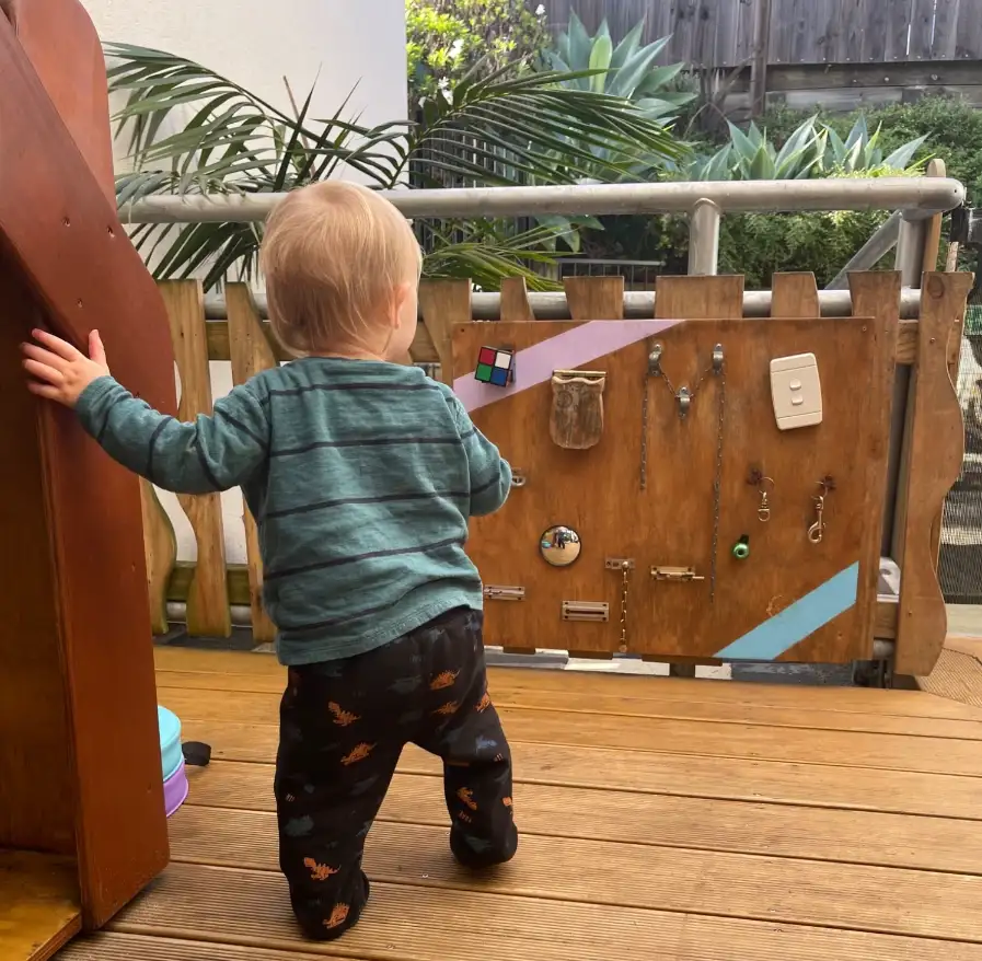 A toddler exploring a wooden discovery board with latches and mirrors on the deck