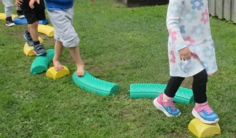 Children balancing across foam stepping stones on the grass