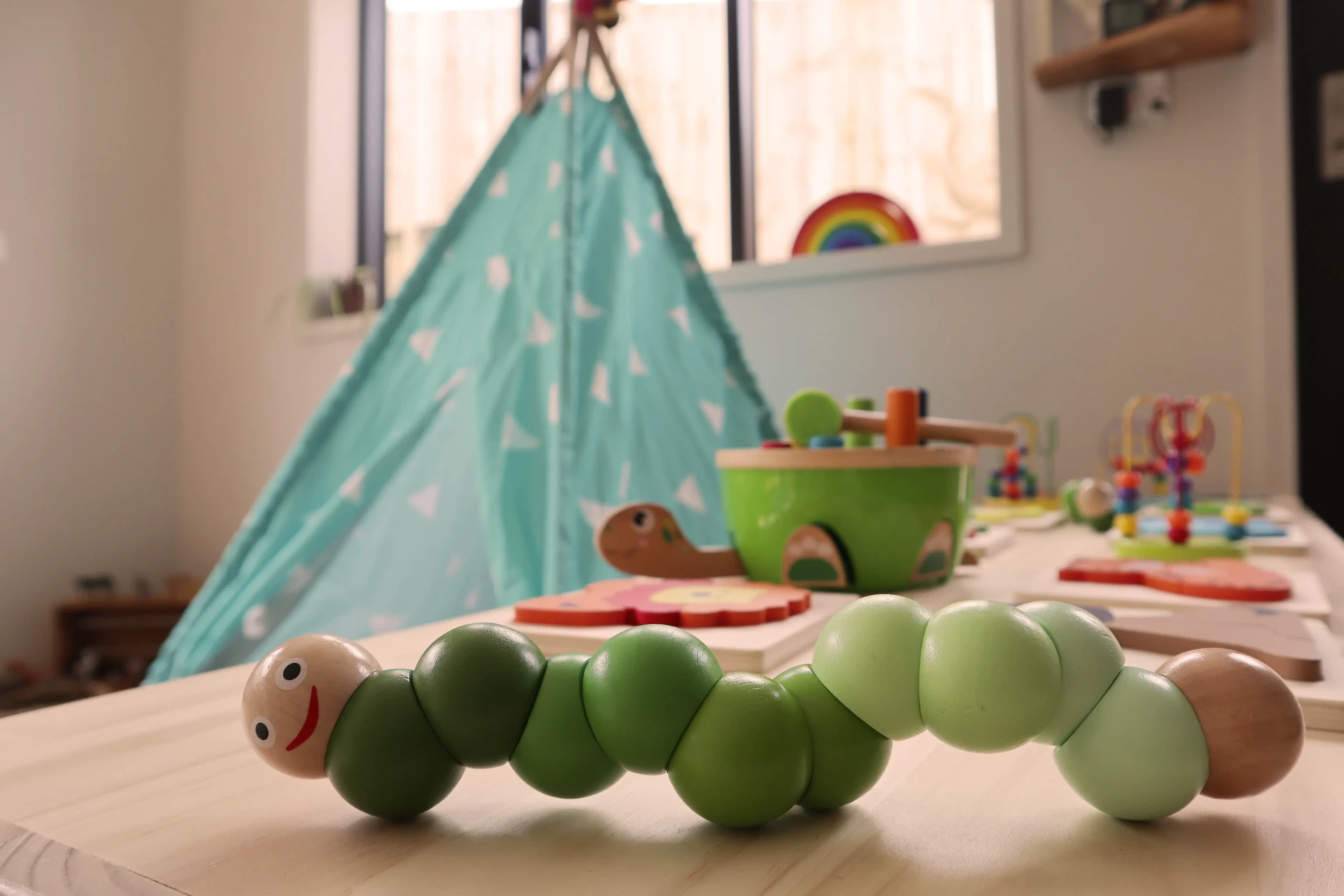 A wooden caterpillar puzzle on a table in front of a teepee in the Bee Room
